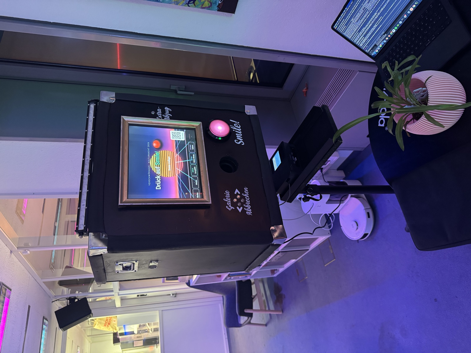 Die Fotobox im Einsatz: schwarzes Flightcase mit goldenem Bilderrahmen um den Touchscreen und großem roten Auslöseknopf